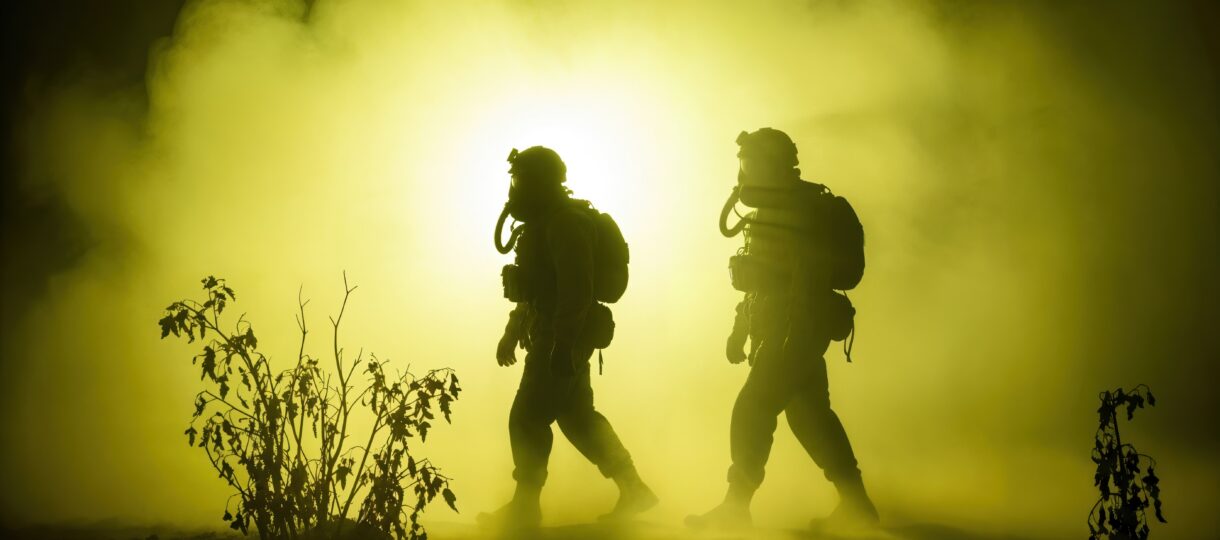 Silhouetted tactical team in gas masks walking through thick yellow chemical gas fog